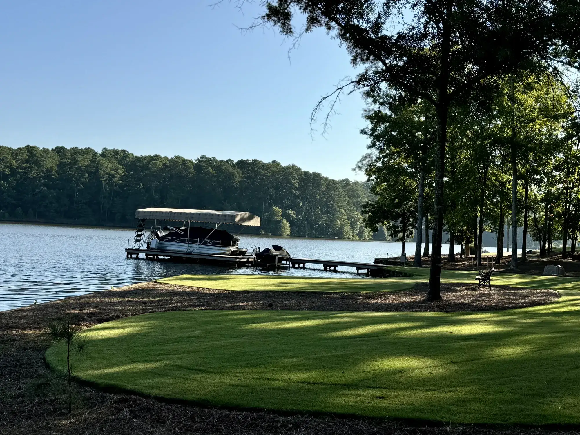A covered dock and pontoon boat on Lake Oconee, with a mown lawn and pines along the shoreline