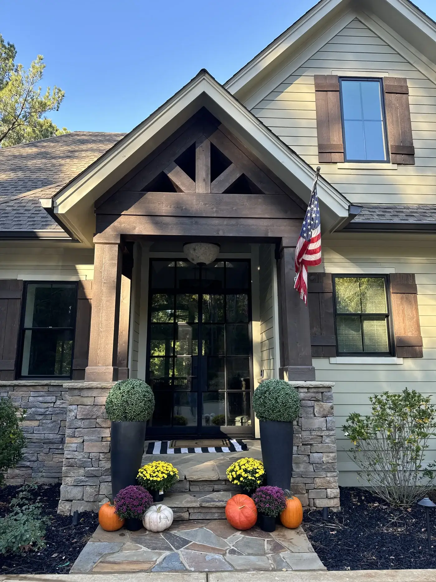 A lake-house front porch decorated for fall with pumpkins and mums